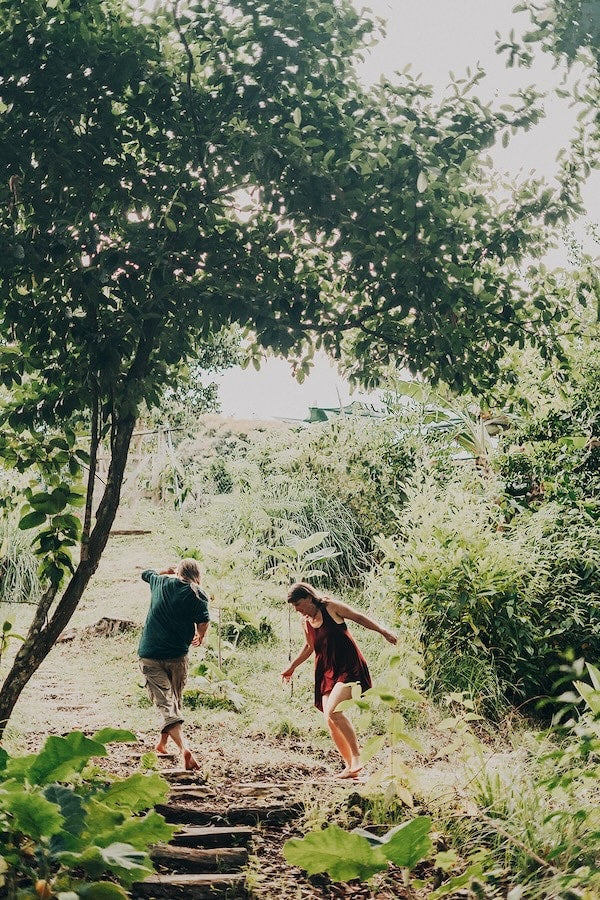 Two people walking the garden paths of the island homestead in golden evening light